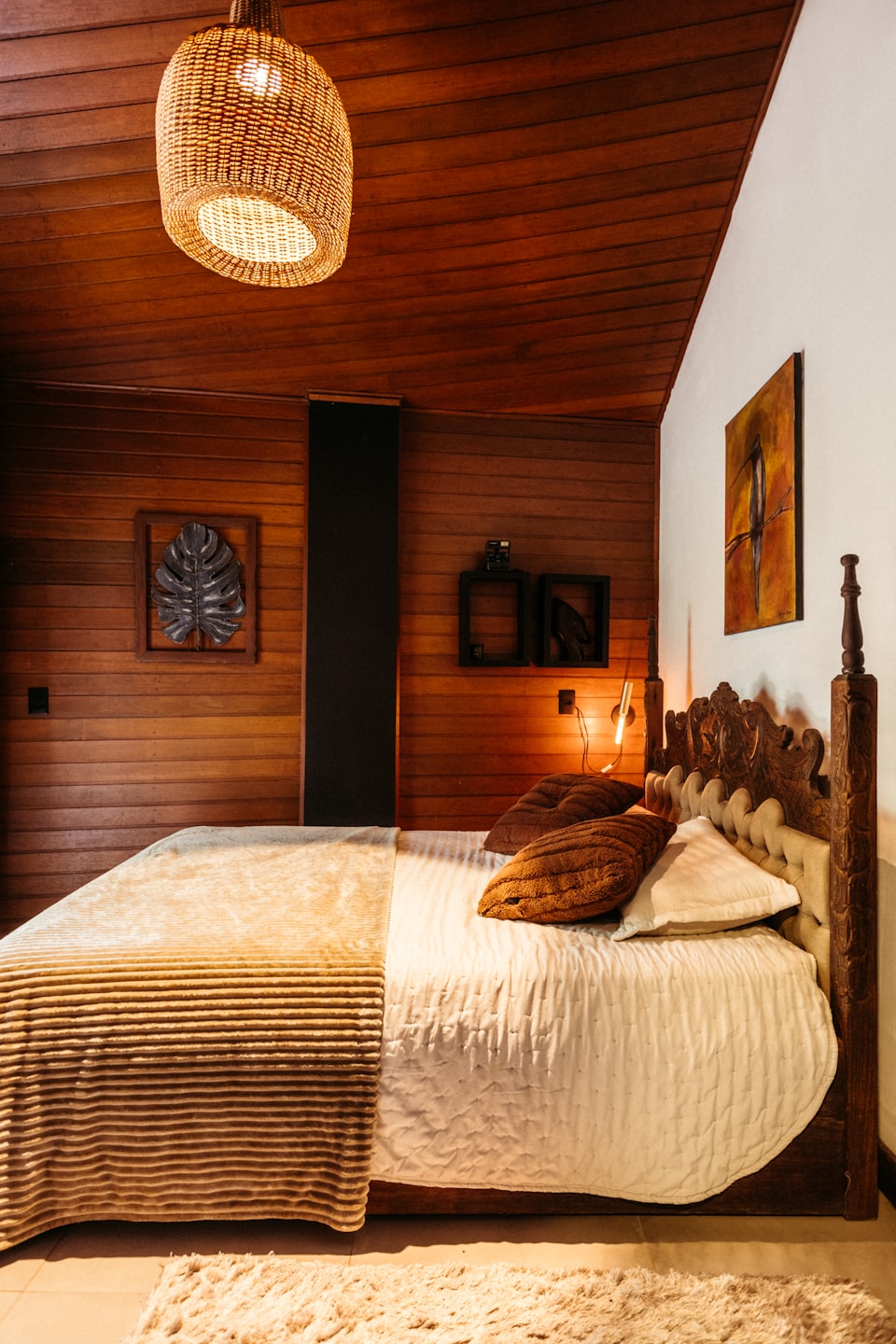 A bed with neutral linens sits in a wooden bedroom.